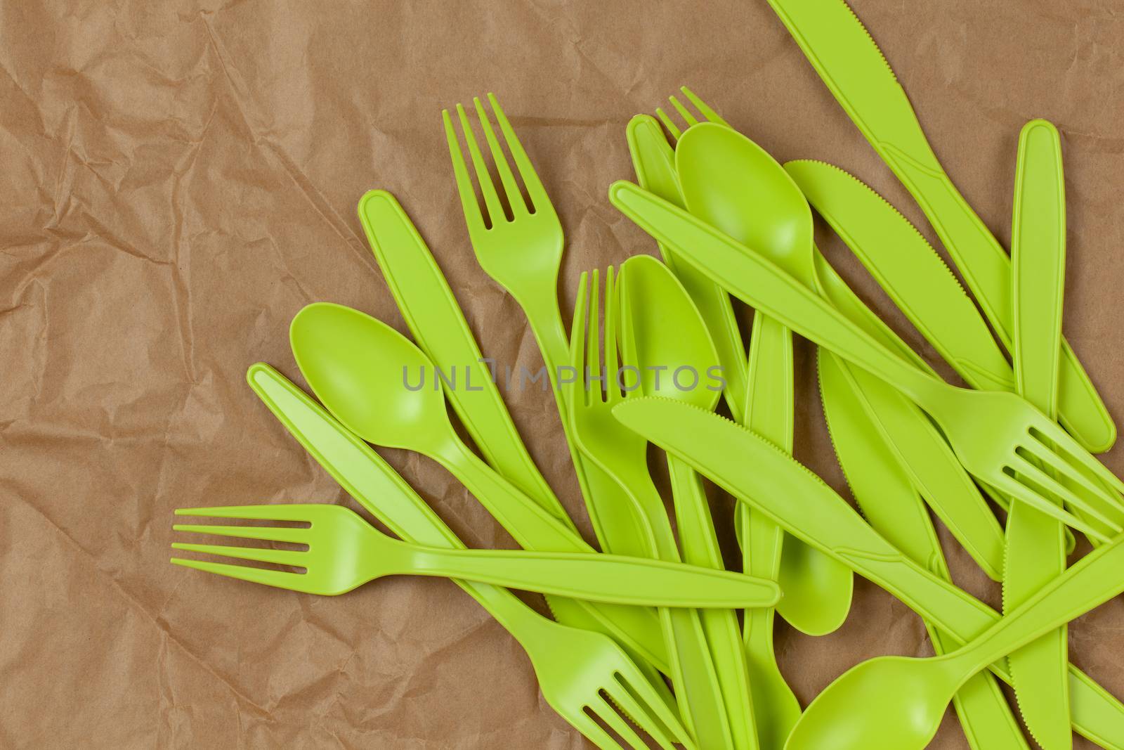 Background from reusable recyclable green forks, spoons, knifes made from corn starch on brown crumpled craft paper. Eco, zero waste, alternative to plastic concept. Flat lay. Horizontal. Closeup.