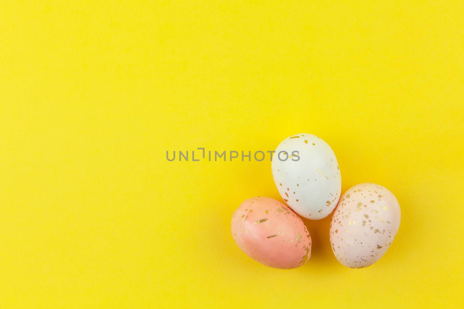 Creatively dyed decorative eggs in pastel colors decorated with gold leaf on yellow background, copy space. Happy Easter do it yourself concept. Flat lay. Horizontal.