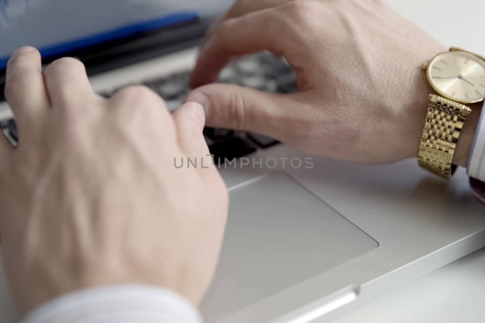 Male hands with gold watch over a laptop keyboard by nyrok