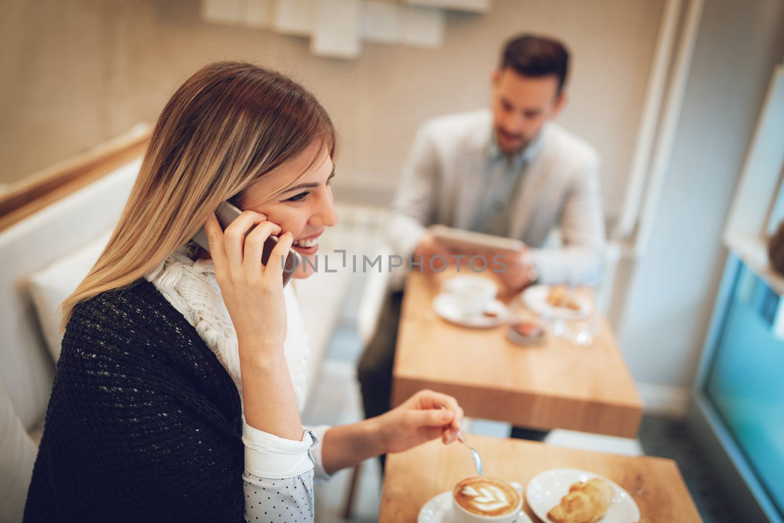 Beautiful young smiling woman using smartphone and drinking coffee in a cafe. Selective focus. Focus on businesswoman.