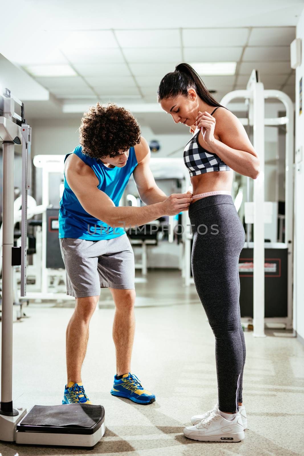 Fitness instructor measuring woman's waist before workout at the gym.
