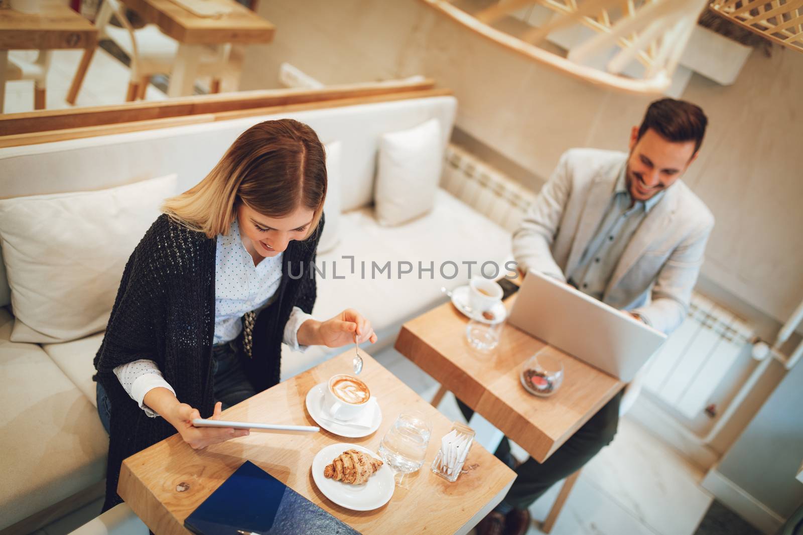 Young businesspeople surfing the internet on a break in a cafe. Smiling woman using digital tablet and drinking coffee. Man working at laptop. Selective focus. Focus on businesswoman.