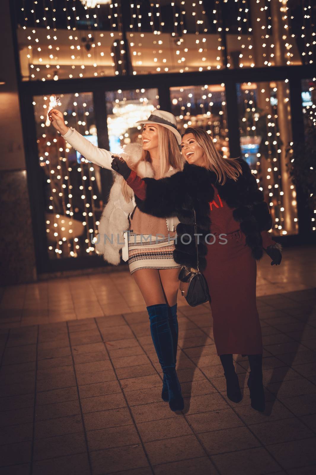 Young beautiful cheerful female friend having fun and walking in the city street at night at Christmas time.