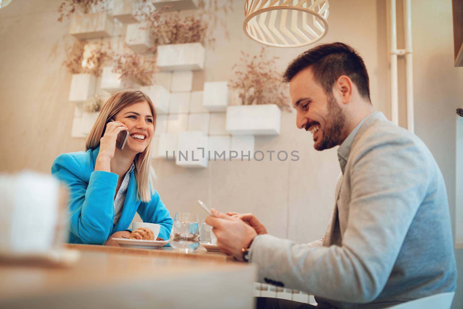 Young businesspeople on a coffee break in a cafe. Smiling woman talking on a smartphone and looking away. Man using digital tablet. Selective focus. Focus on businesswoman.