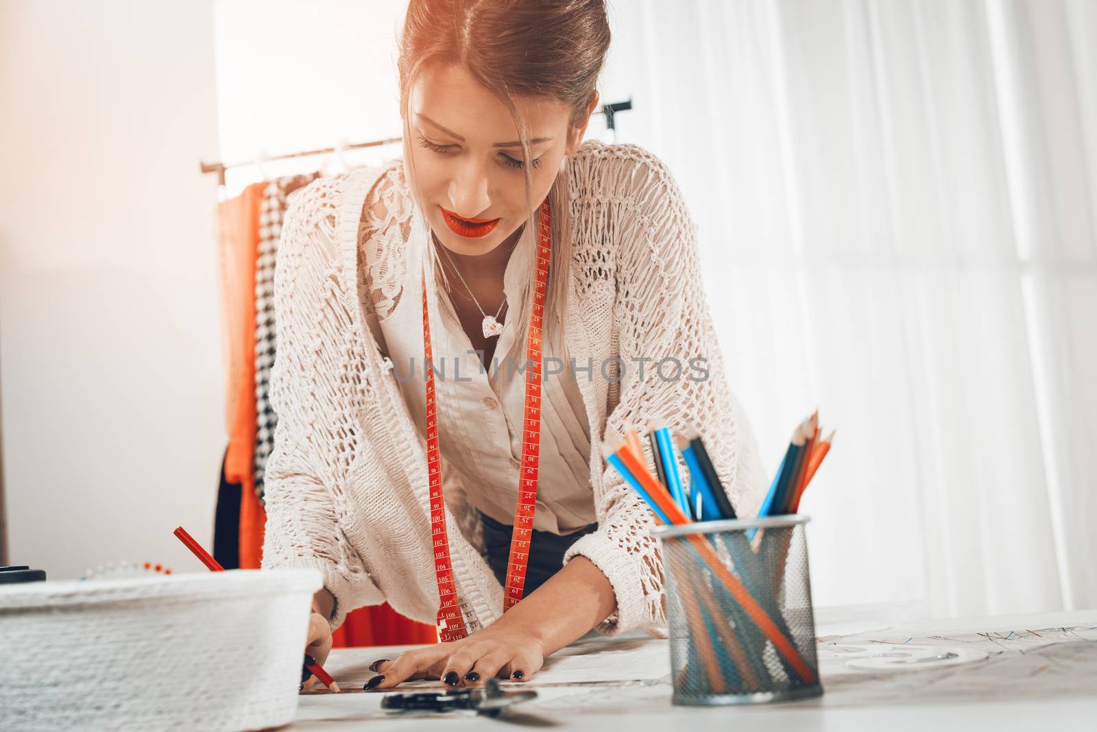 Young female fashion designer with tape measure draped over the neck drawing on sewing pattern with a ruler.