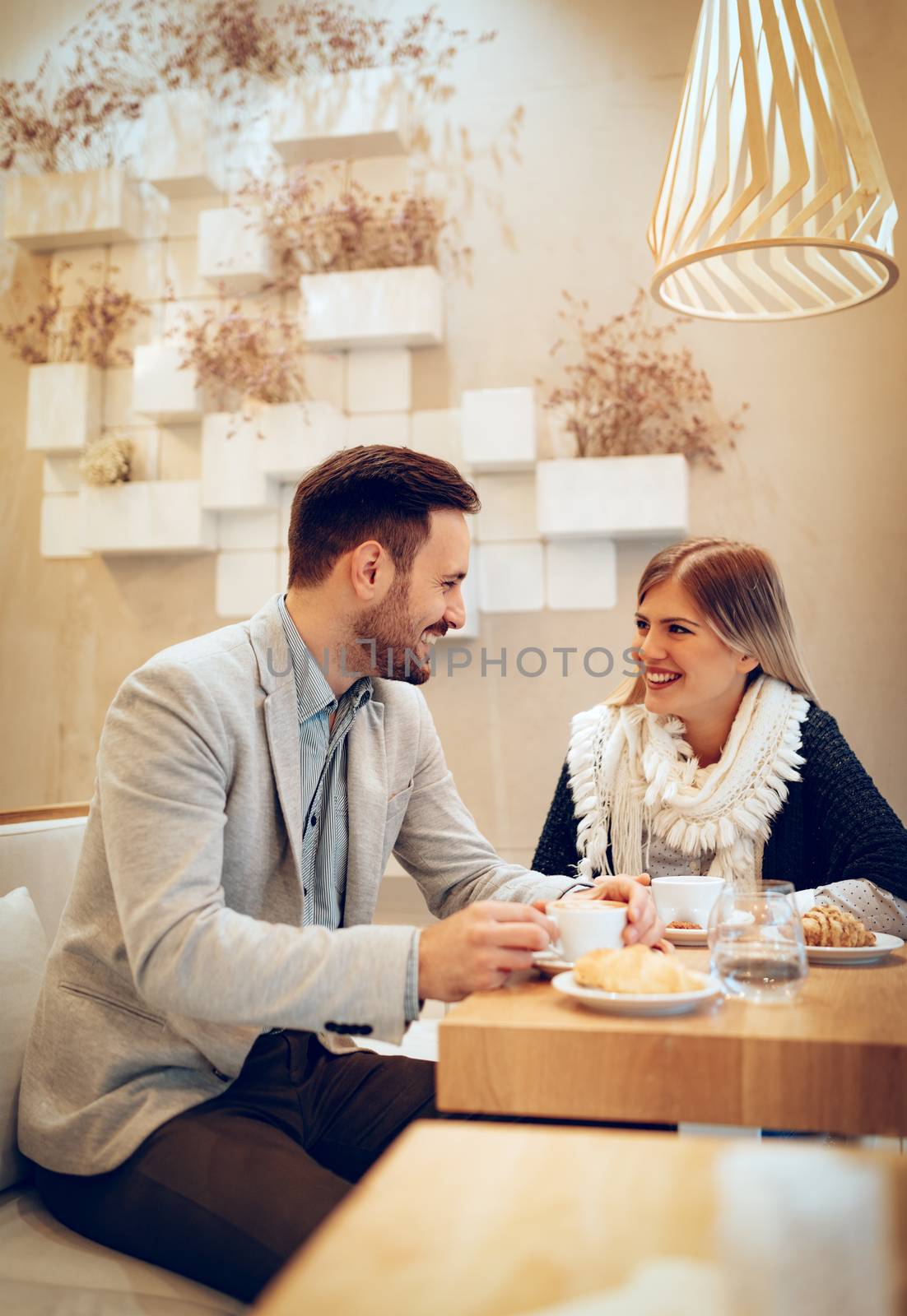Young man and young woman sitting at cafe and talking with smile. 