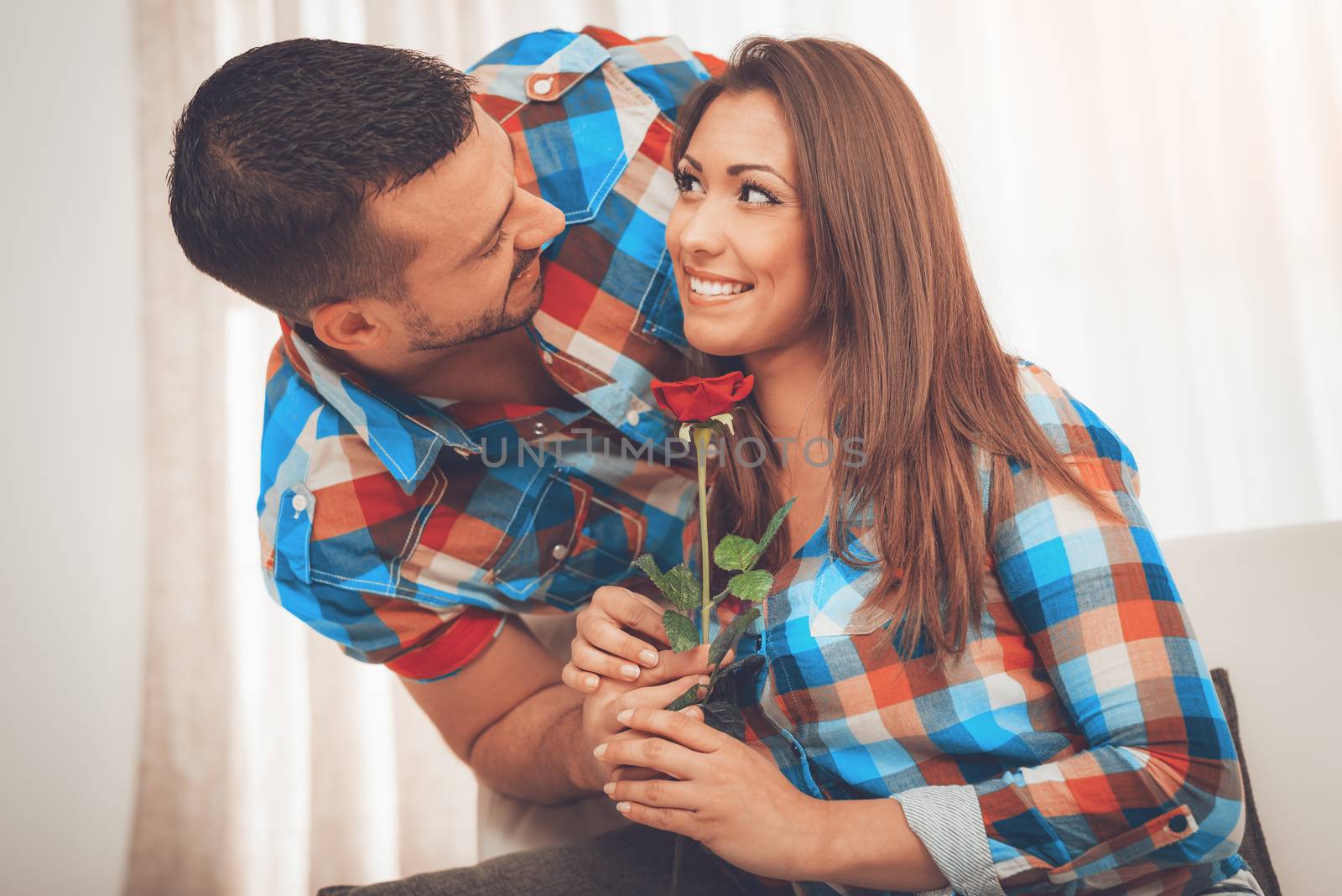 Handsome young man in love give red rose to his girlfriend in an apartment.