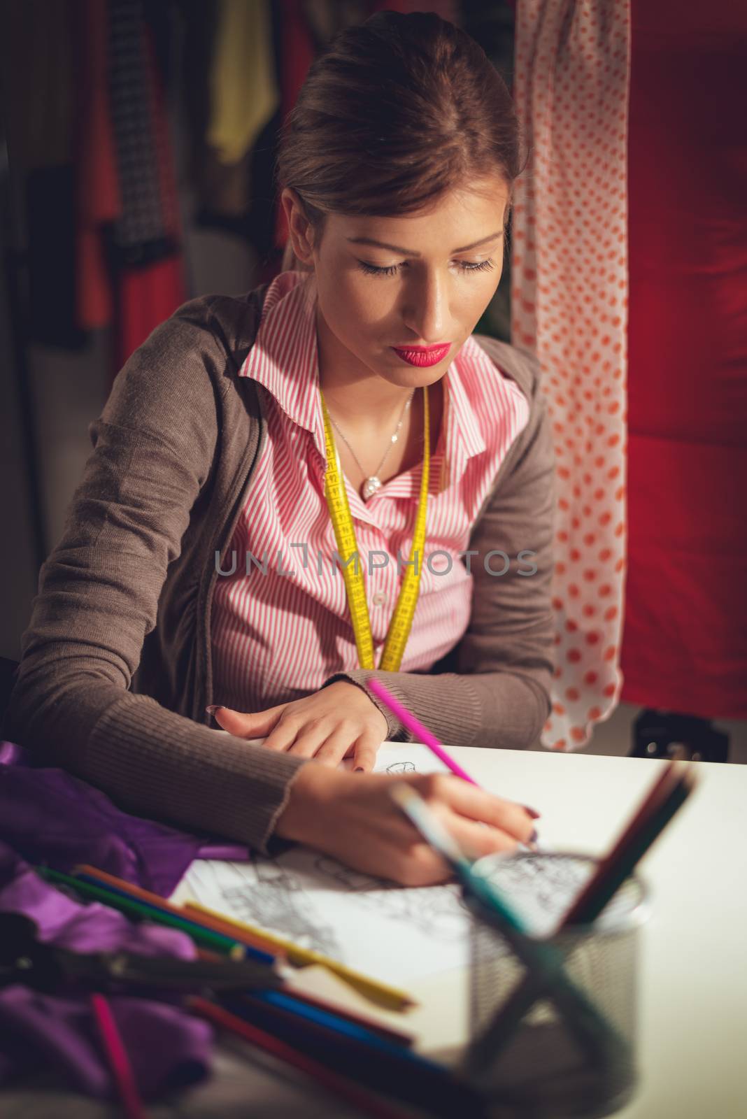 Young female tailor with tape measure draped over the neck drawing on sewing pattern.