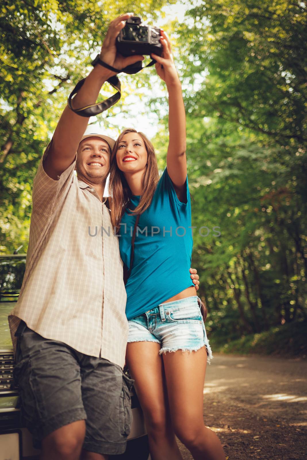 Young travelers standing before a car in the forest and taking photo of themselves.