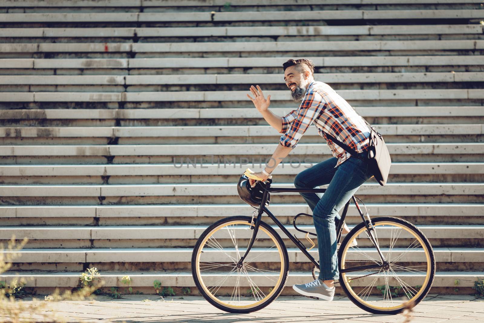Casual handsome businessman going to work by bicycle. He is riding bike and waving Hello.
