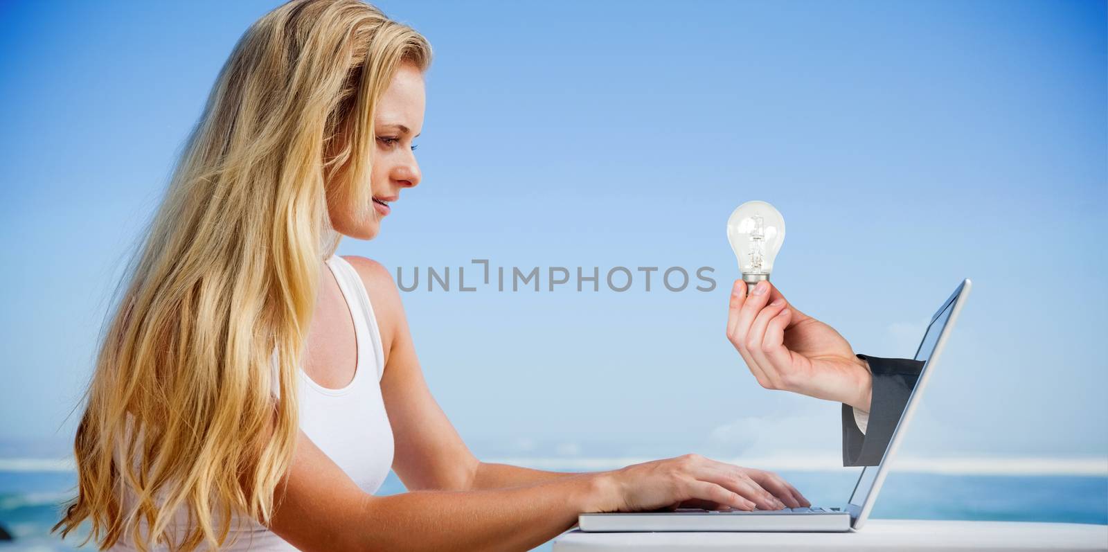 Composite image of pretty blonde using her laptop at the beach with hand holding bulb