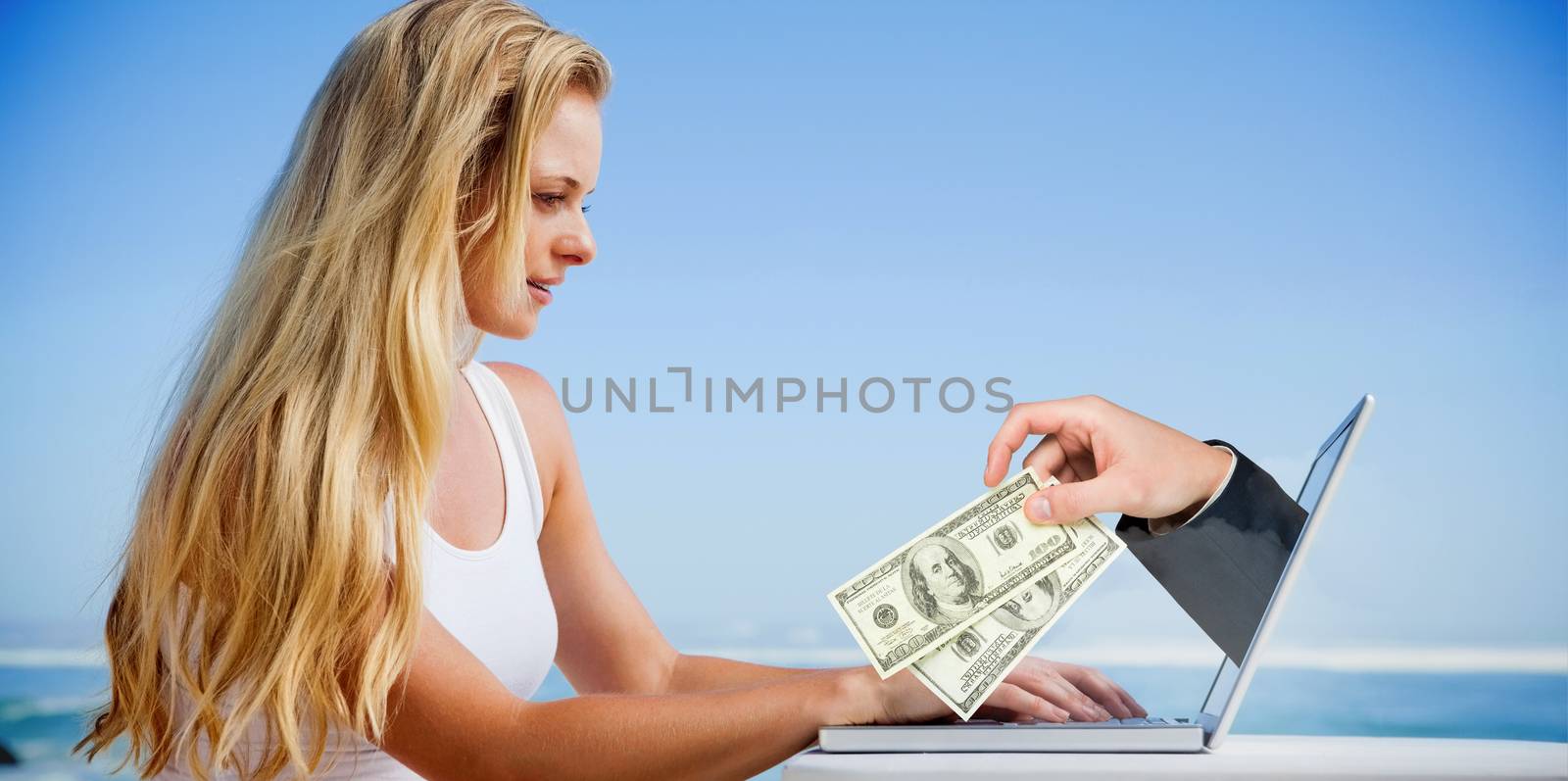 Composite image of pretty blonde using her laptop at the beach with hand holding money