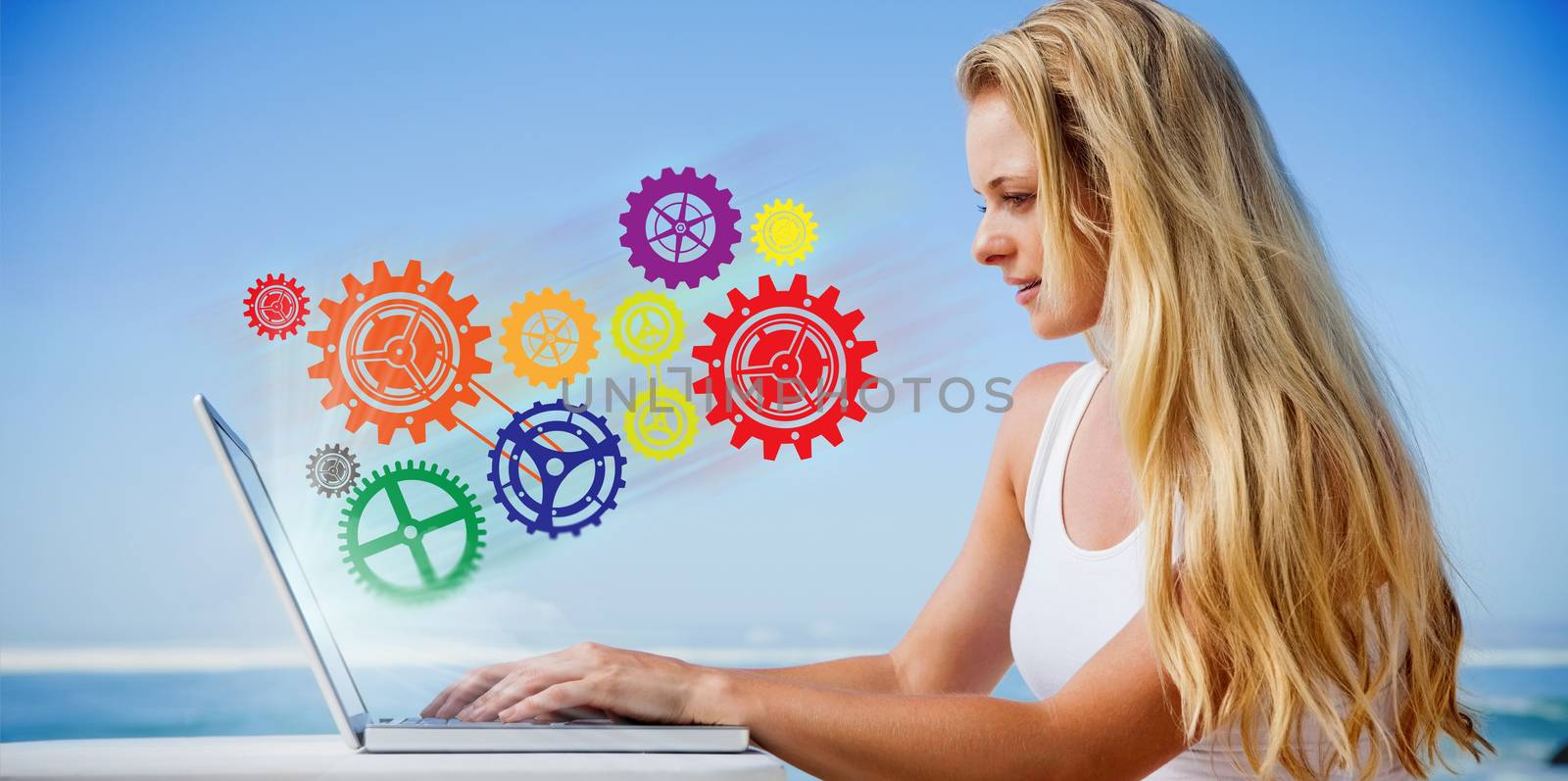 Pretty blonde using her laptop at the beach against cogs and wheels