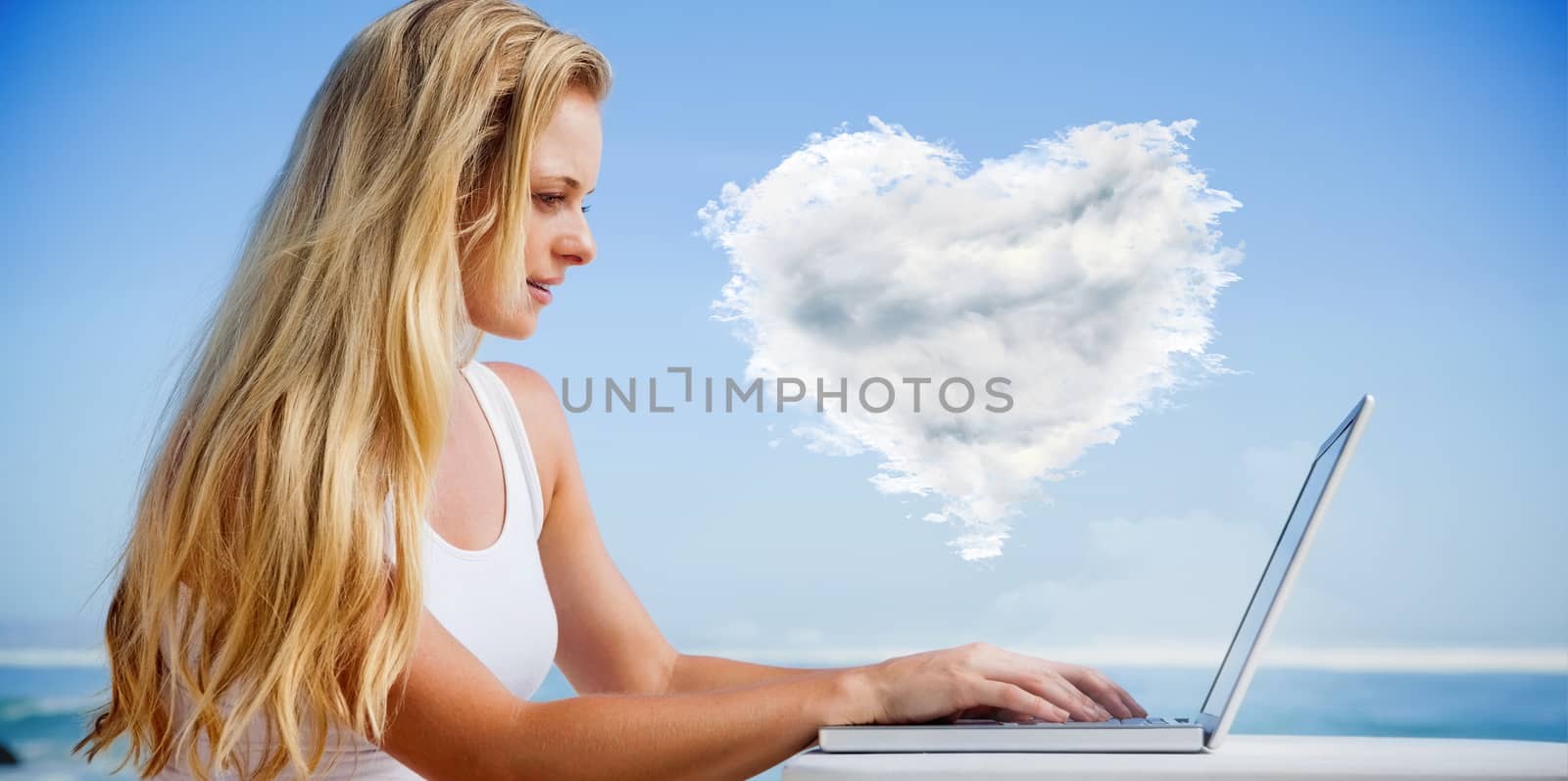 Composite image of pretty blonde using her laptop at the beach against cloud heart