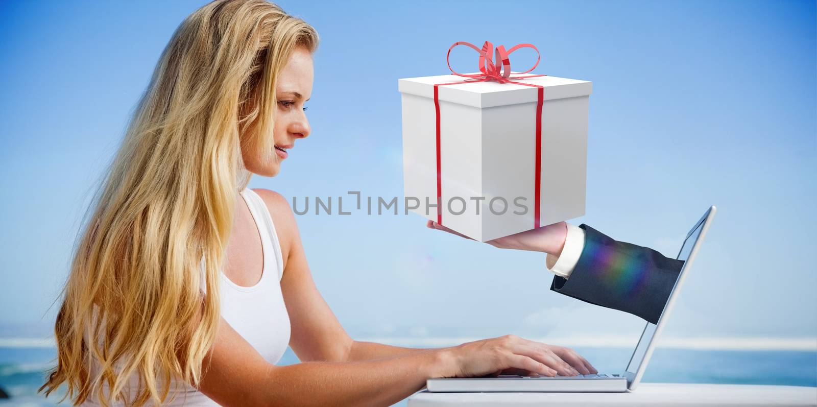 Composite image of pretty blonde using her laptop at the beach with hand holding gift