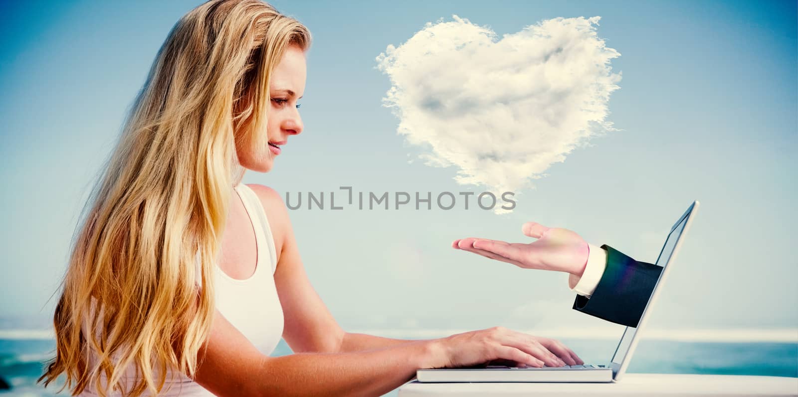 Composite image of pretty blonde using her laptop at the beach with hand presenting cloud heart