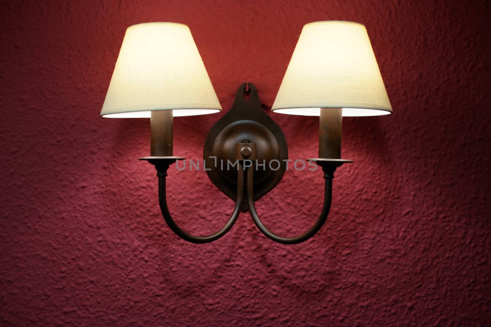 Yellow light coming from a two bulb wall sconce presented on a pink wall, vintage style.