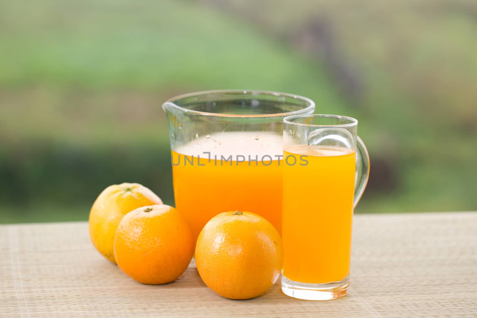 glass of delicious orange juice and oranges on table in garden