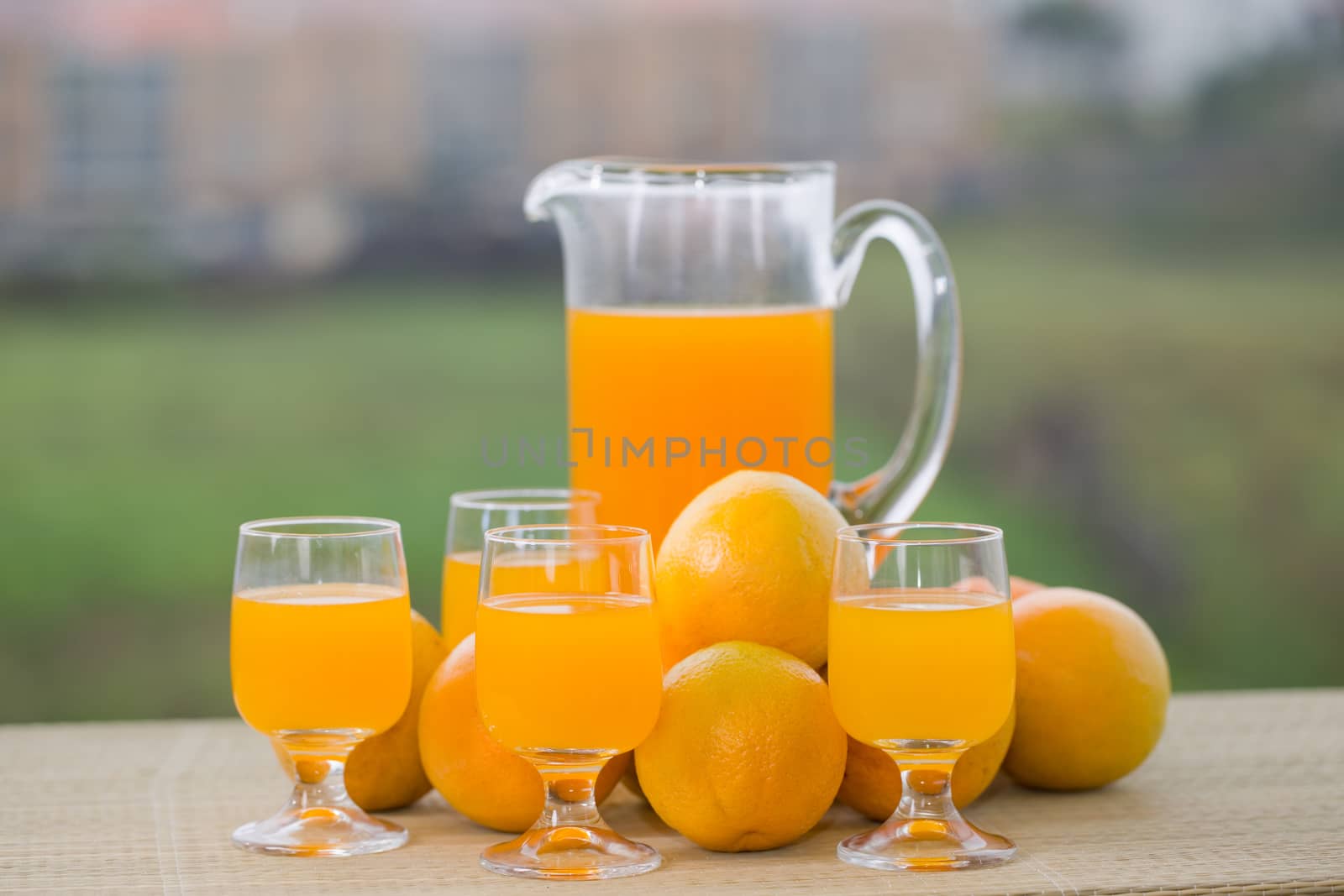 glass of delicious orange juice and oranges on table in garden