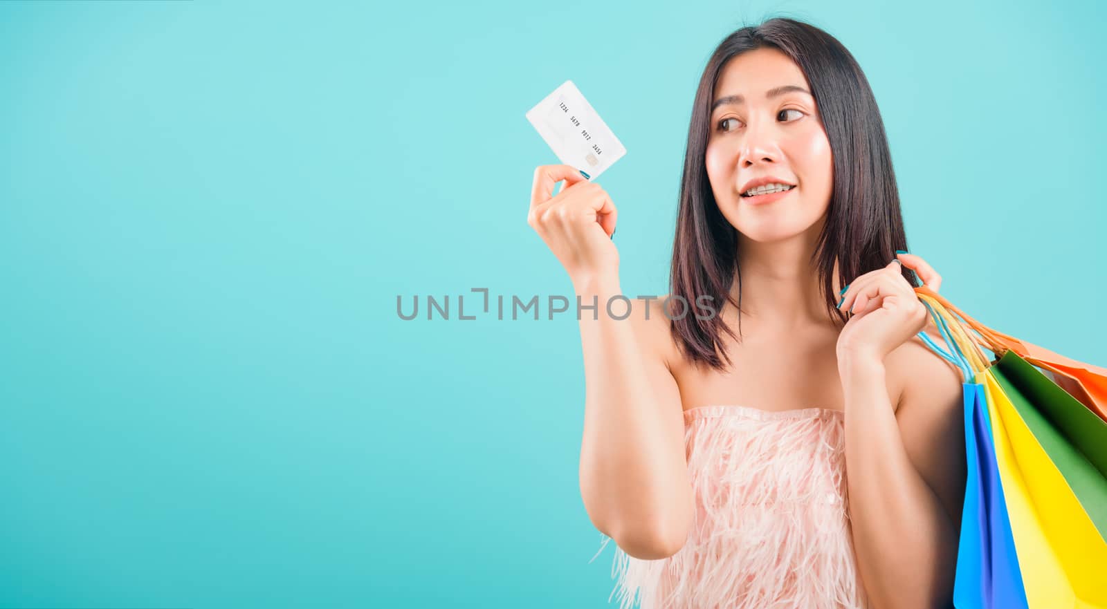 Portrait asian beautiful woman smiling holding shopping bags and credit card and her looking to credit card on blue background, with copy space for text
