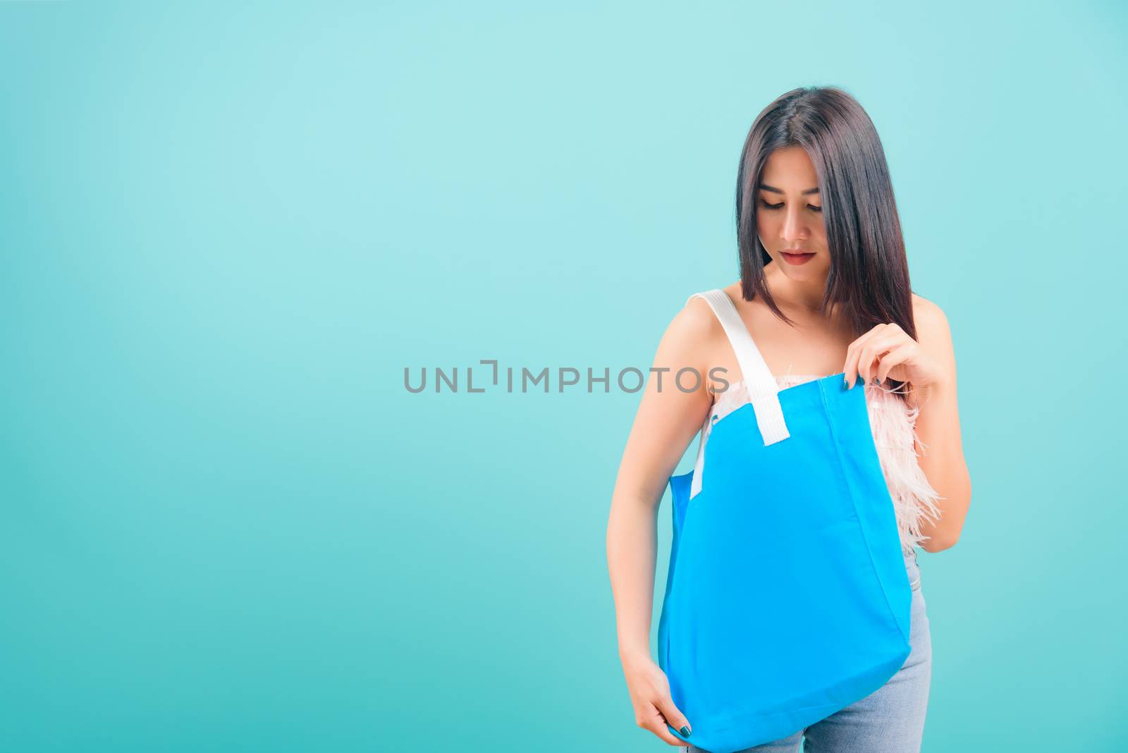 Smiling face portrait asian beautiful woman holding eco blue fabric bag on blue background, with copy space for text