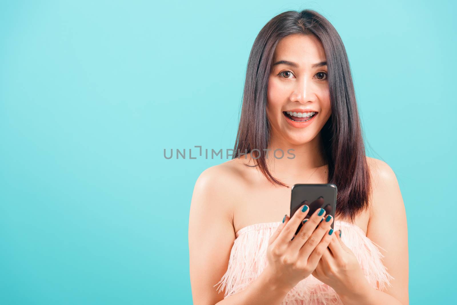 Smiling face portrait asian beautiful woman standing using mobile phone her excited on blue background, with copy space for text