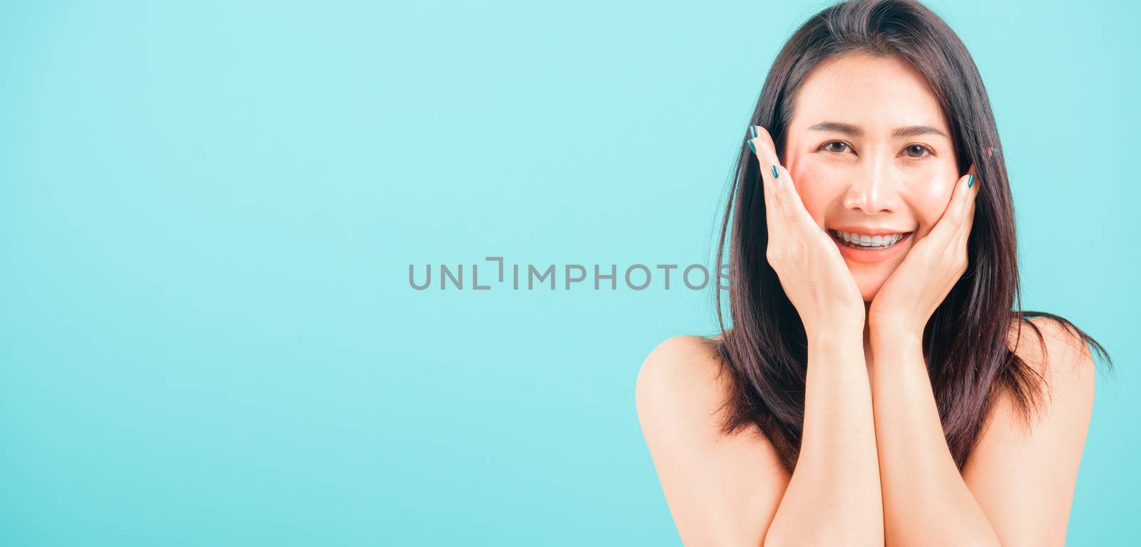 Smiling face Asian beautiful woman her hands touch on face skin on blue background, with copy space for text