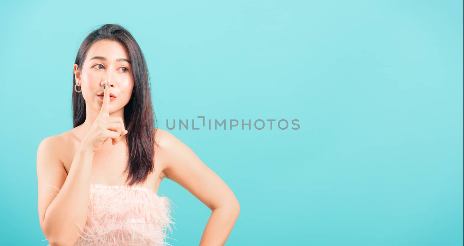 Smiling face Asian beautiful woman her asking quiet with finger on lips pointing with hand on blue background, with copy space for text