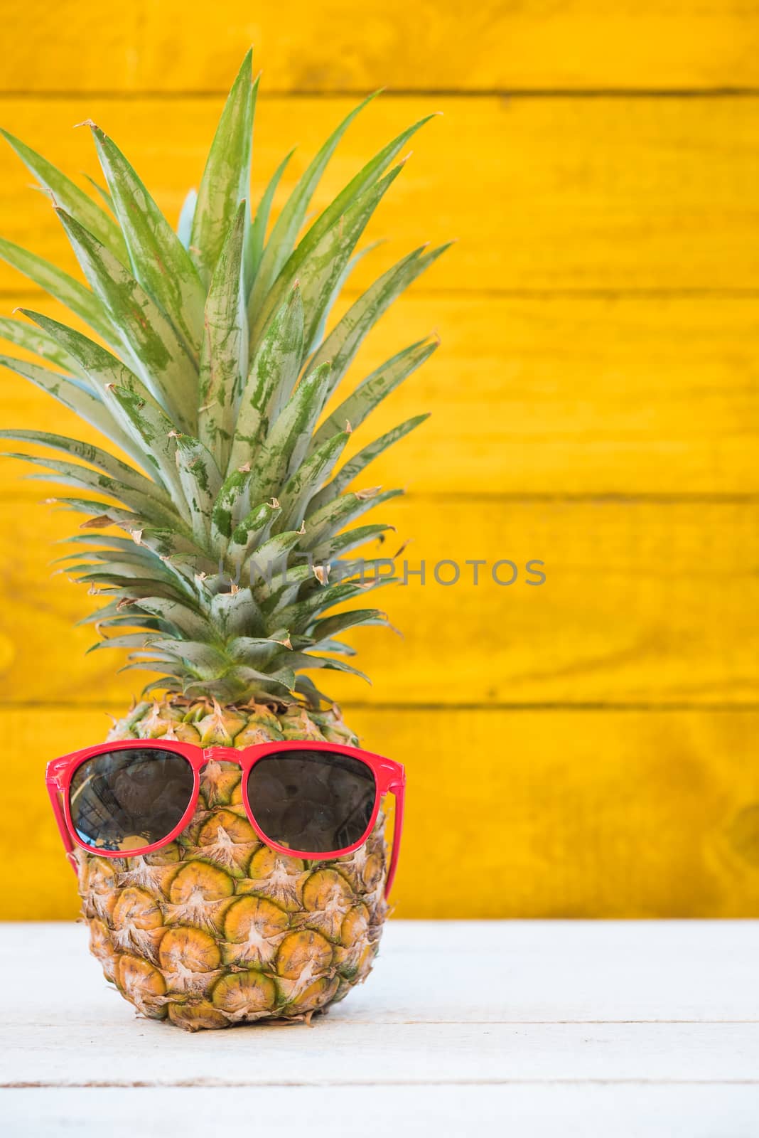 Holiday pineapple have sunglasses on yellow wooden background, tropical holiday concept