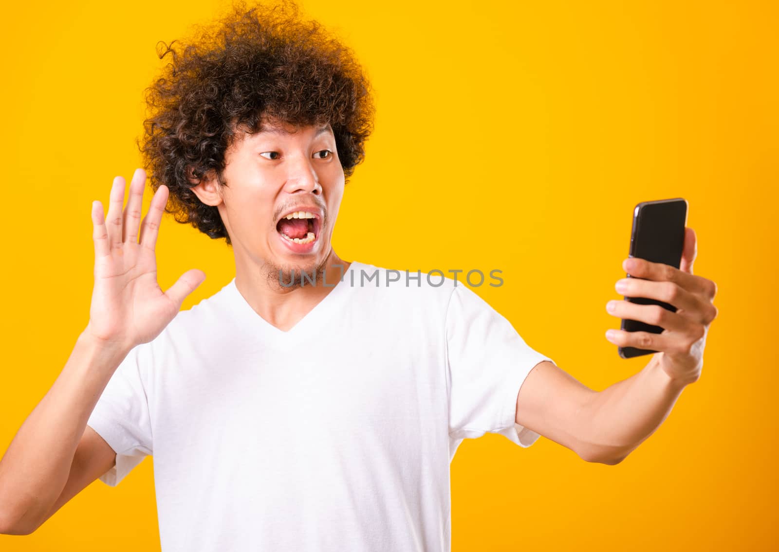 Portrait asian handsome man curly hair taking selfie with mobile phone isolated on yellow background