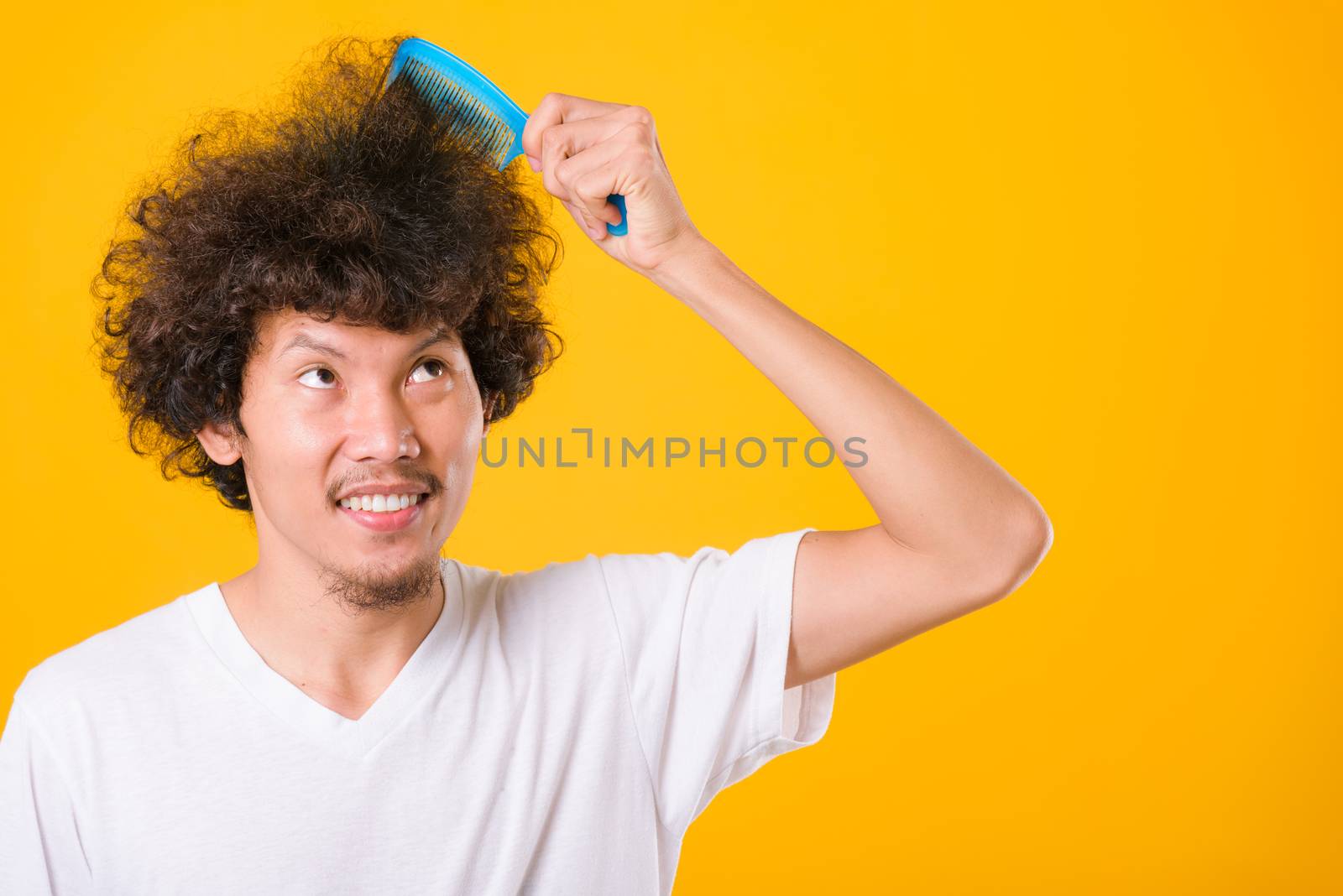 Asian man combing curly hair on yellow background with copy space for text
