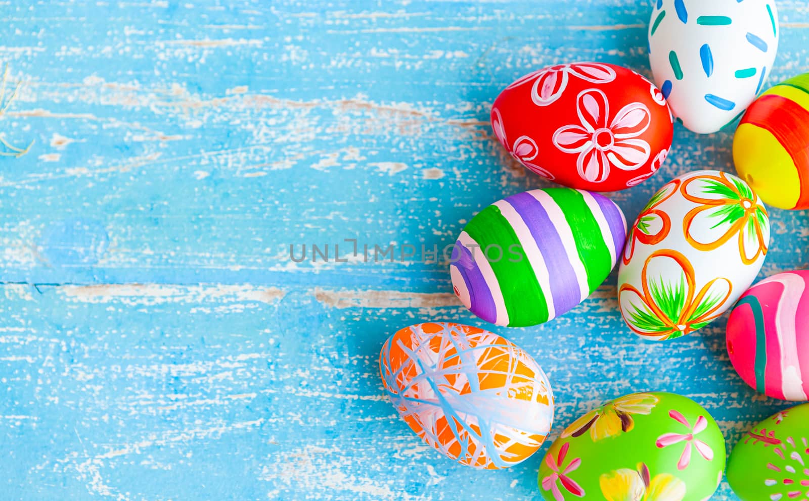 Easter eggs in various designs and colors are placed on a pastel blue wooden background with copy space for fall during Easter.