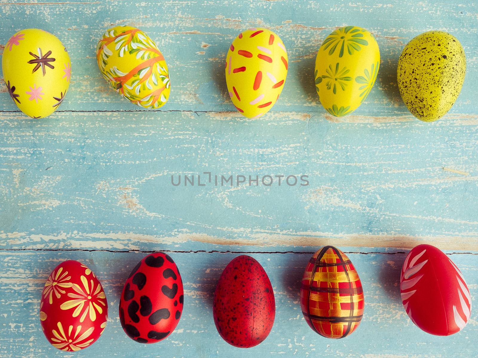 Easter eggs are arranged in two rows between yellow and red on a pastel blue wood floor. Vintage style coloring