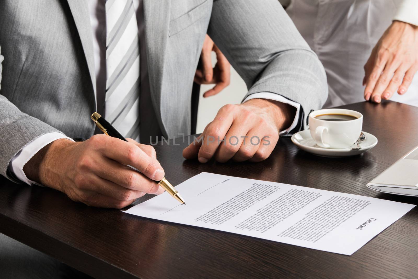 Businessman in gray suit sitting at office desk signing a contract close up