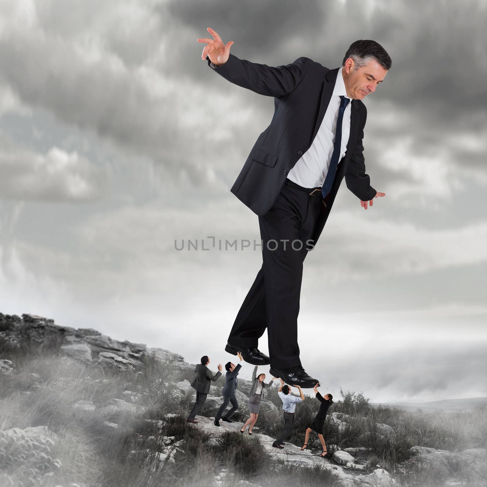 Composite image of business team supporting boss against rocky landscape