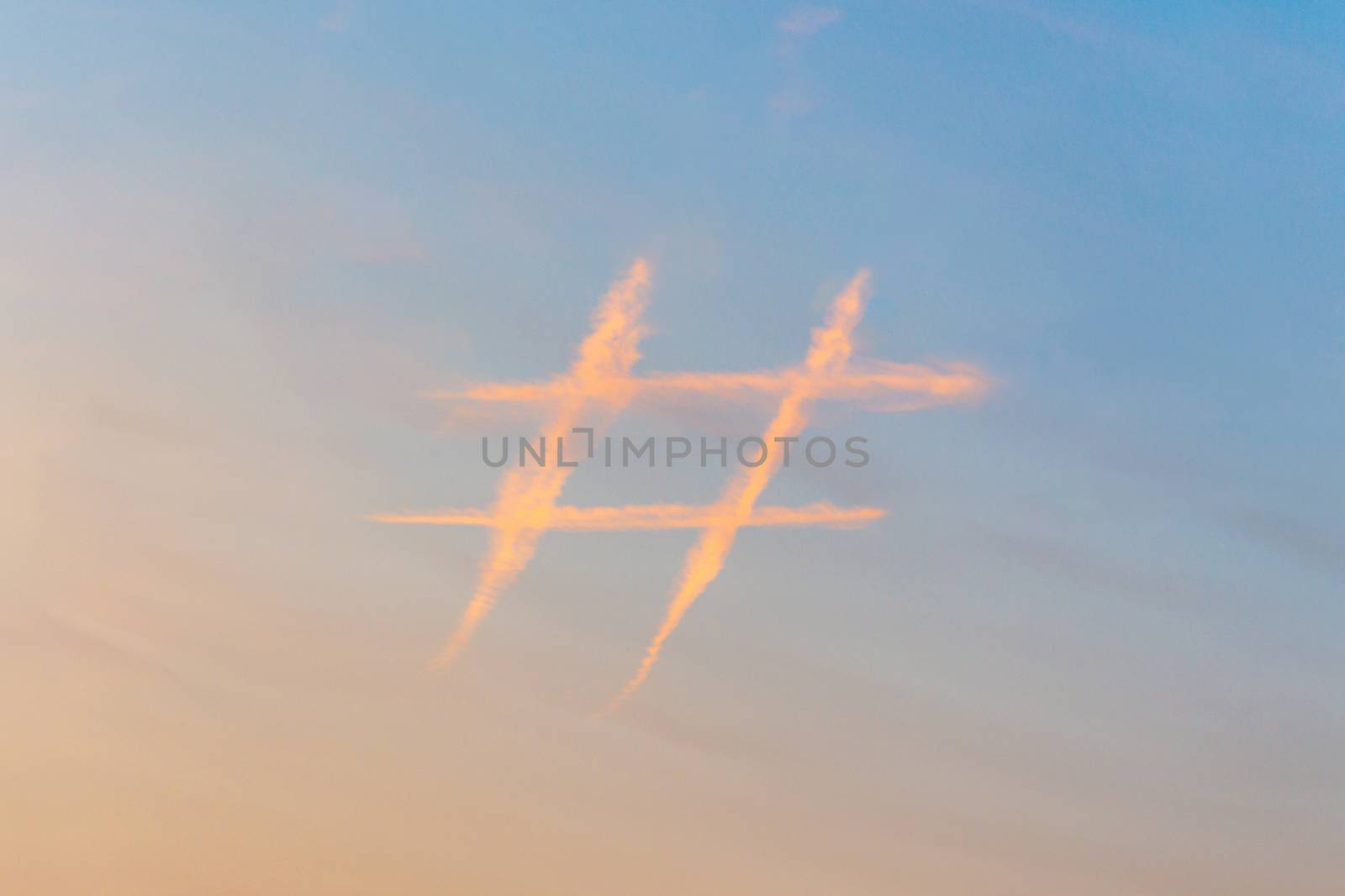 Hashtag sign in sky at sunset, icon made out of contrail clouds. Social media and microblogging concept.