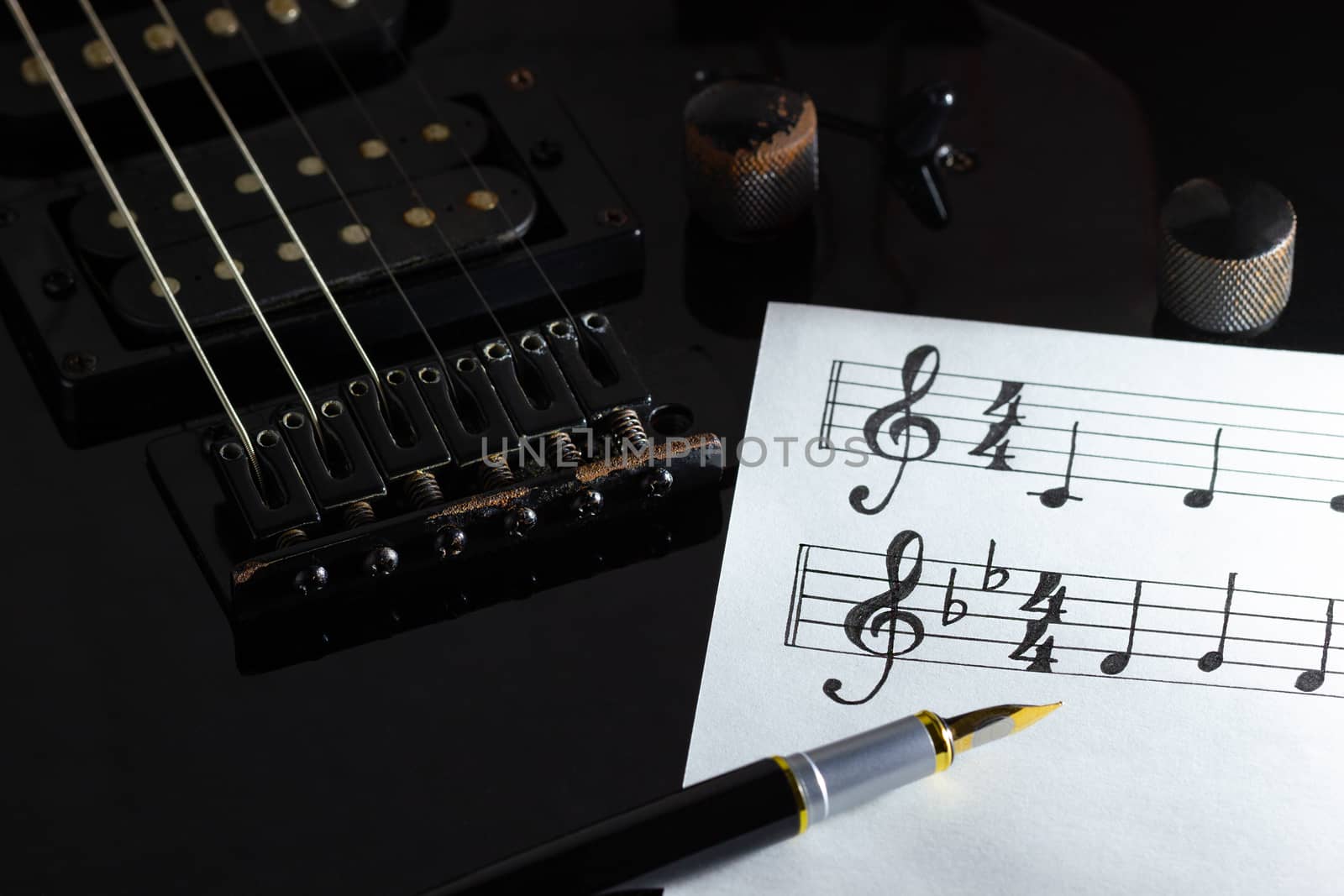 Music note and vintage pen on black electric guitar in darkness. by SaitanSainam