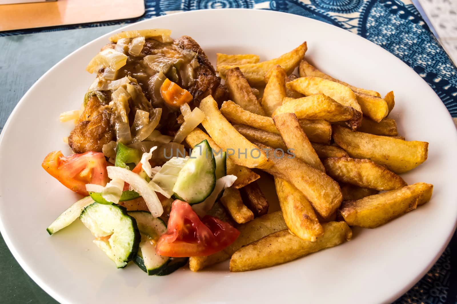 Baked chicken leg with fries and vegetables on a white plate and a blue tablecloth.