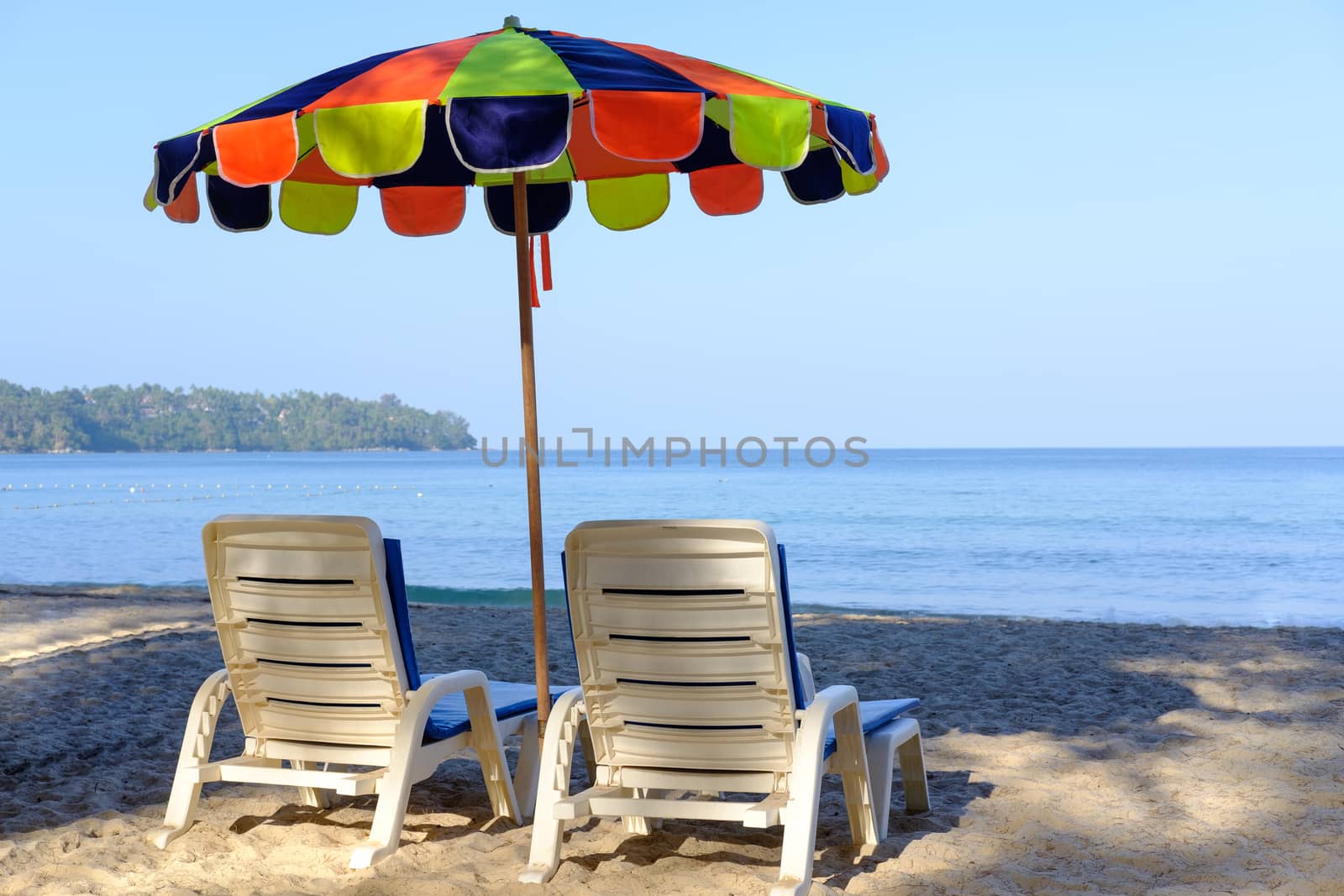 Beach bed and cheerful colorful parasol on tropical beach with blue sky and blue sea. Closeup of Back view beach chairs and umbrella for  summer vacation and holiday concept. 