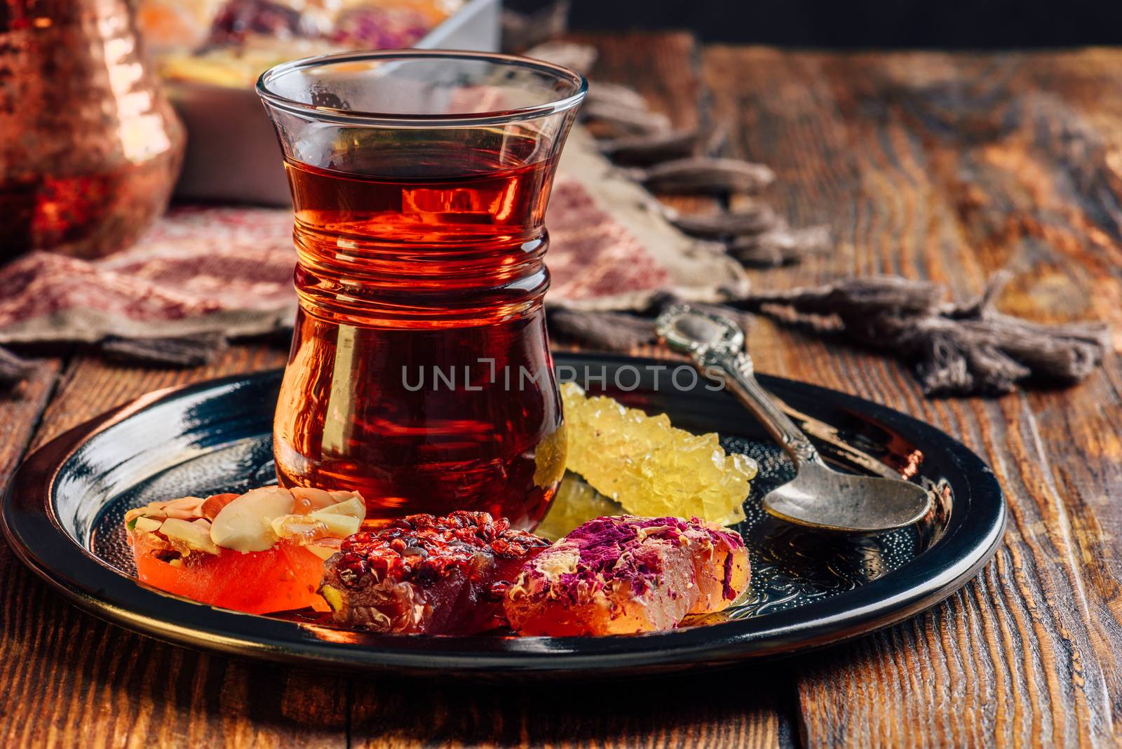 Tea in armudu glass with oriental delight rahat lokum on metal tray over wooden surface and tablecloth