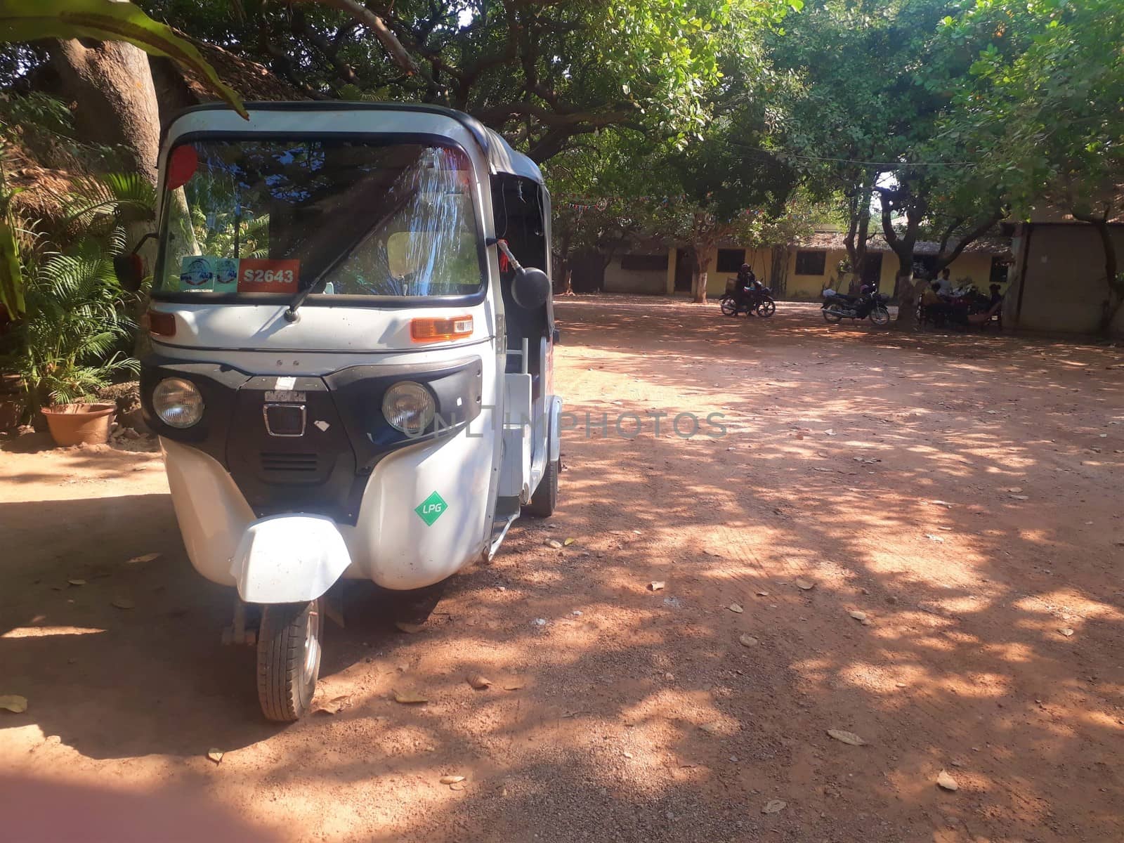 A tuk tuk parked on a dirt road.