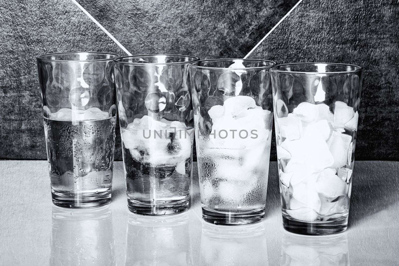 Monochrome view of four glasses of ice on a table top, each at a different stage of melting.