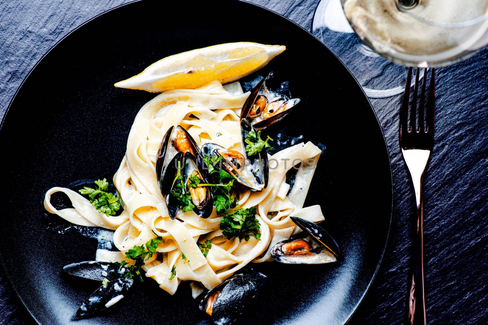 Blue mussels and pasta in black plate on stone surface