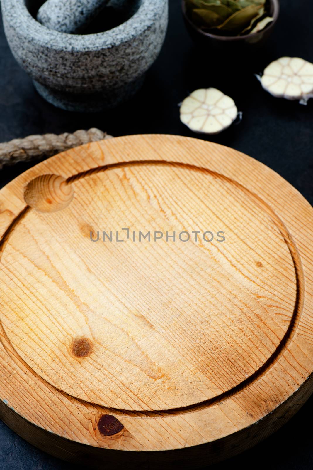 Stone mortar bowl with pestle, garlic, bay leaf and wooden cutting board on stone surface