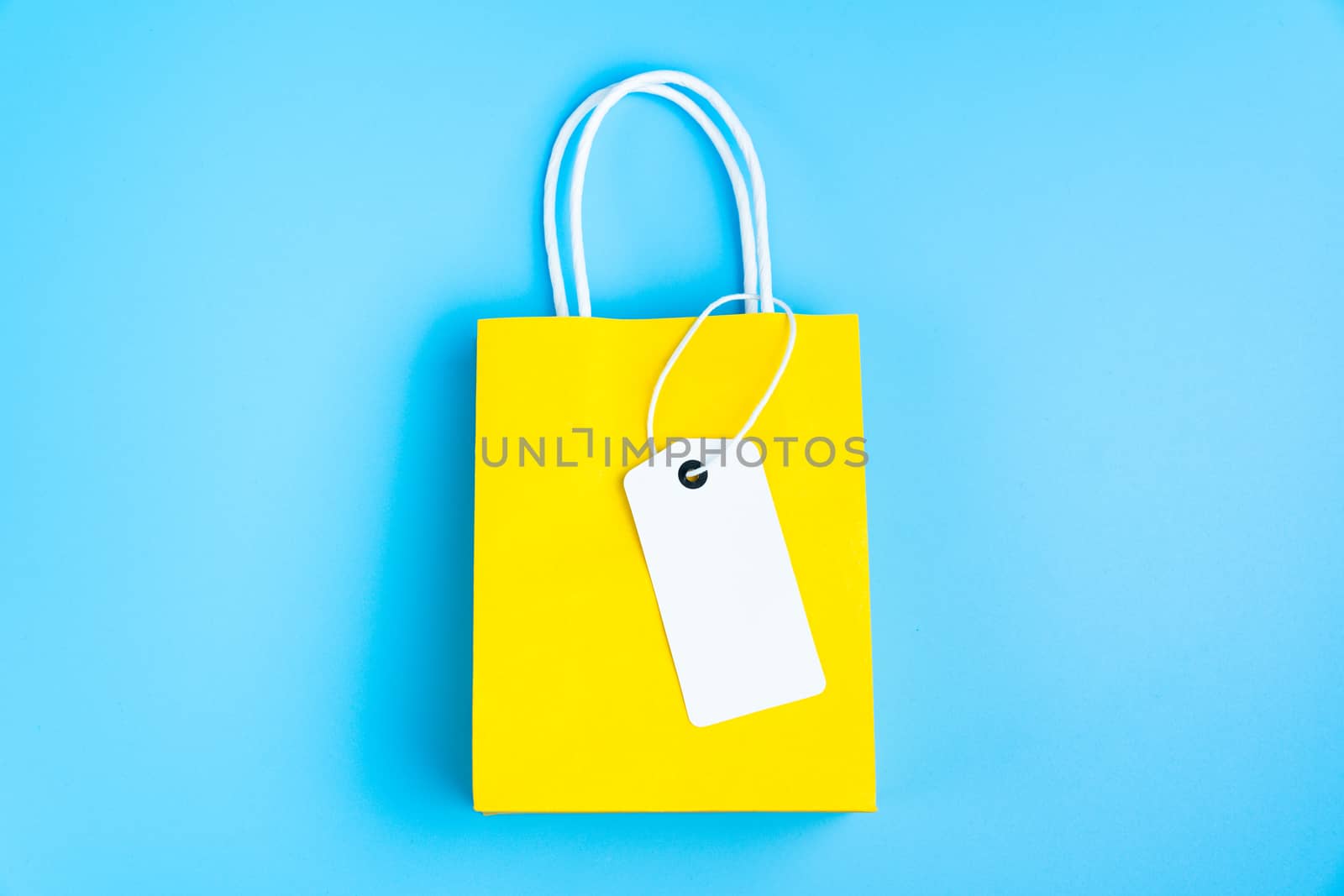 Single yellow gift or shopping bag with blank label tag isolated on blue background