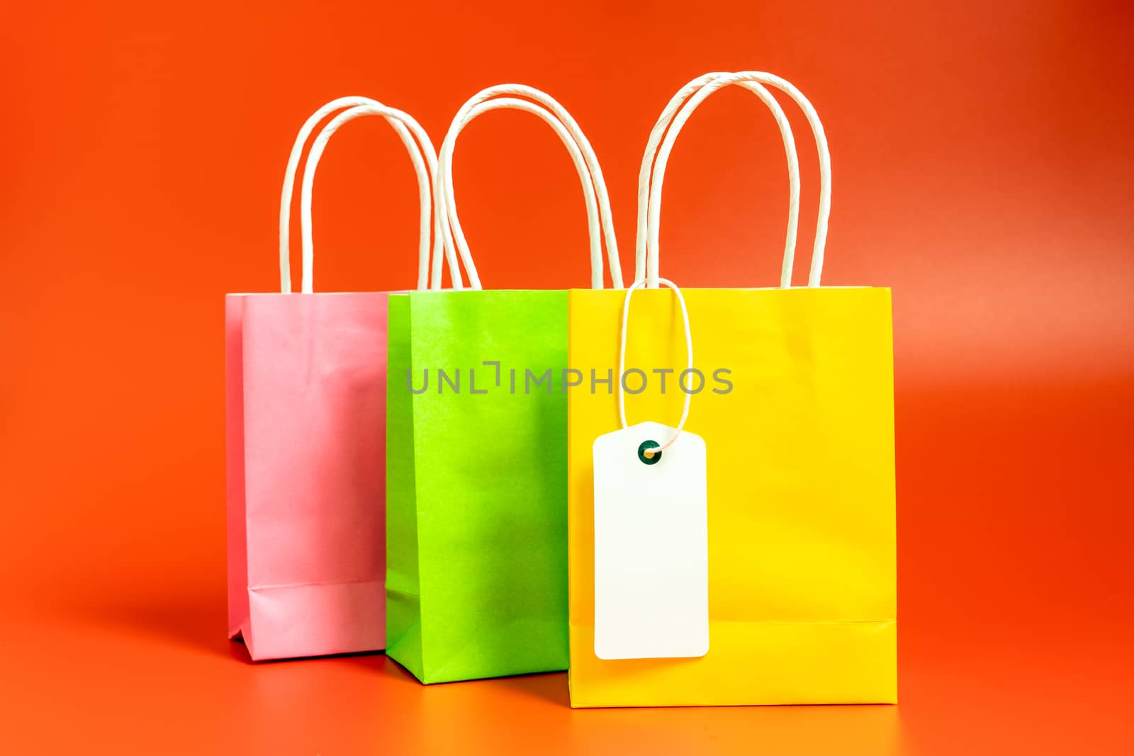 Yellow, green and pink gift or shopping bags with blank tag isolated on red background