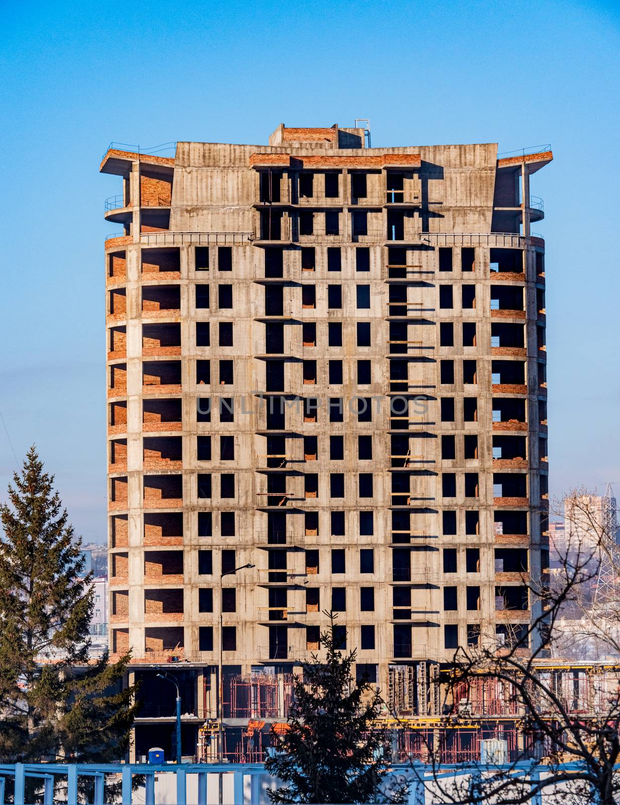 Concrete high-rise building under construction on blue sky background. by Imagenet
