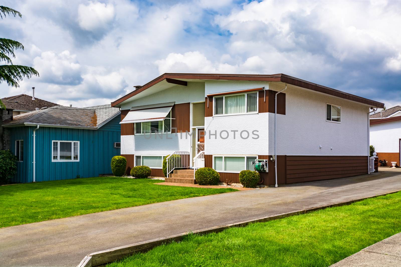 Family house with green lawn in front. Average residential house on cloudy day in British Columbia