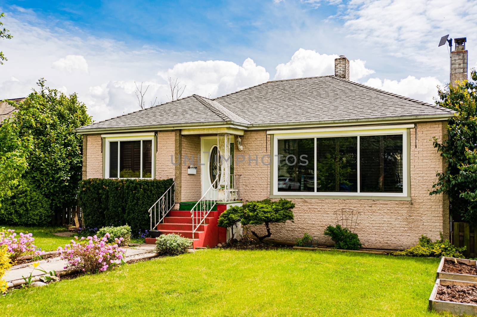 Modest family house with green lawn in front and stone wall texture. Old residential house on cloudy day in Canada