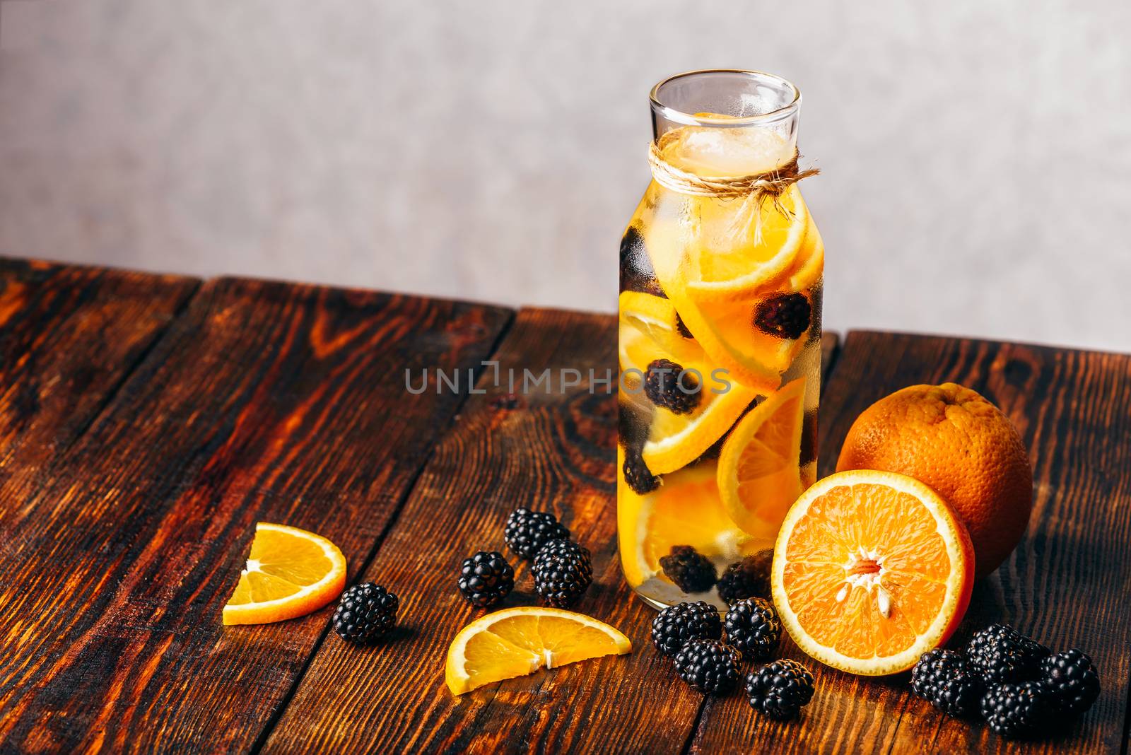 Bottle of Water Infused with Sliced Raw Orange and Fresh Blackberry. Ingredients on Wooden Table.